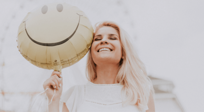femeie cu zâmbet perfect care ține un balon cu smily face